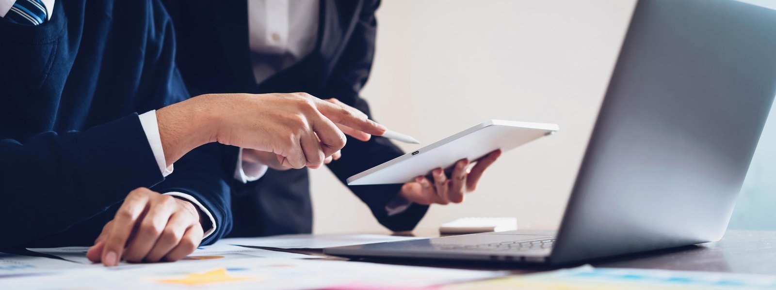 Two business people reviewing figures on a tablet and laptop